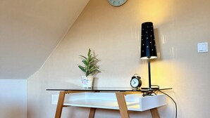 Ett rum med ett sluttande tak, ett skrivbord med en klocka, en lampa och en liten växt.