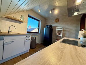 A modern kitchen with a window, white cabinets, a black refrigerator, and a wooden countertop.
