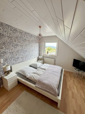 A bedroom with a bed, nightstands, a lamp, a television, and a window with a view.
