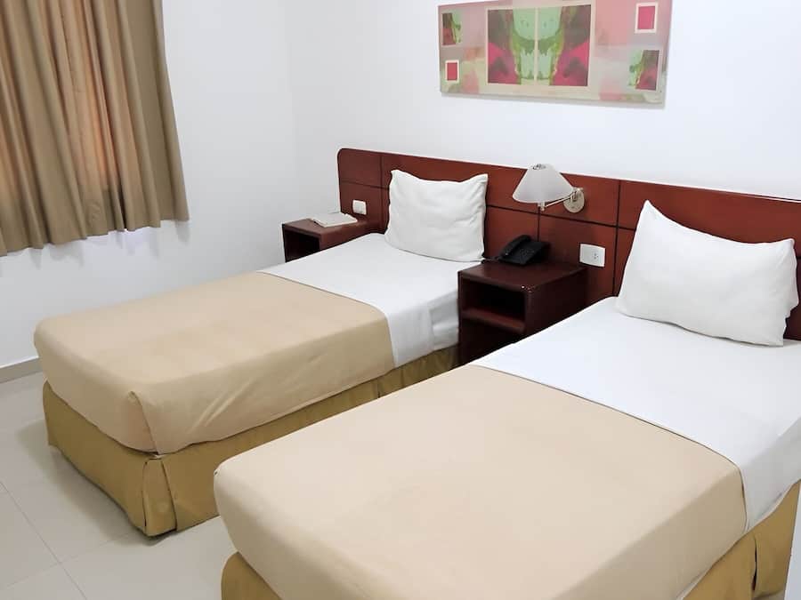 A hotel room with two beds, a nightstand with a phone, a lamp, and a wall-mounted air conditioner.