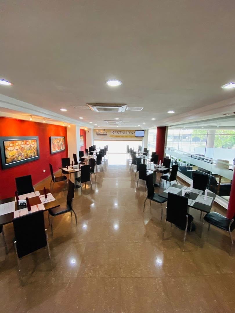 A restaurant with tables and chairs arranged in rows, a red wall with artwork, and a view through large windows.