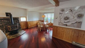 Una habitació amb una llar de pedra, panells de fusta, una taula de dinar amb caires i un quadre floral gran a la paret.