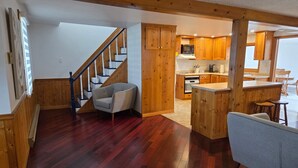 Un vaste espace de vie agrémenté d’un escalier en bois, une cuisine avec des meubles en bois et un coin repas doté d’un bar.