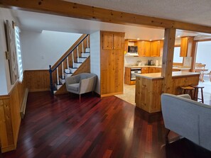 A spacious living area with a wooden staircase, a kitchen with wooden cabinets, and a dining area with a bar. - Lakefront Cottage in the Heart of Kincardine | 3 BR | 2 Baths | 2 Decks (Kincardine)