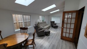 A spacious living room with a sofa, chairs, a dining table, and a large window. - Lakefront Cottage in the Heart of Kincardine | 3 BR | 2 Baths | 2 Decks (Kincardine)