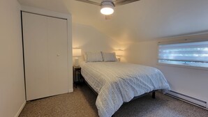 Une chambre à coucher comprenant un lit, une armoire, une fenêtre avec des stores et un ventilateur de plafond.