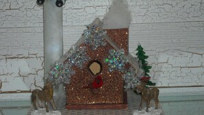 Uma cena natalina em miniatura, com uma casa, renas e um boneco de neve.