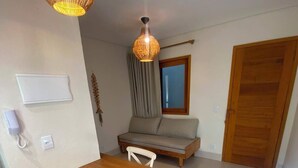 A dining area with a wooden table and chairs, a hanging light fixture, a sofa, and a wooden door. - Sueds Vila Romana (Porto Seguro)