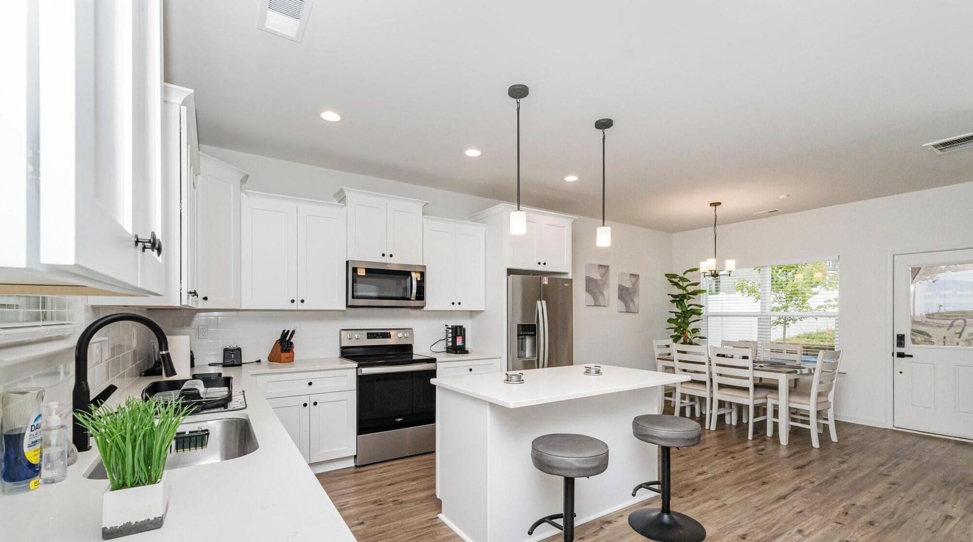 A modern kitchen with white cabinetry, stainless steel appliances, a central island with bar stools, and pendant lighting.