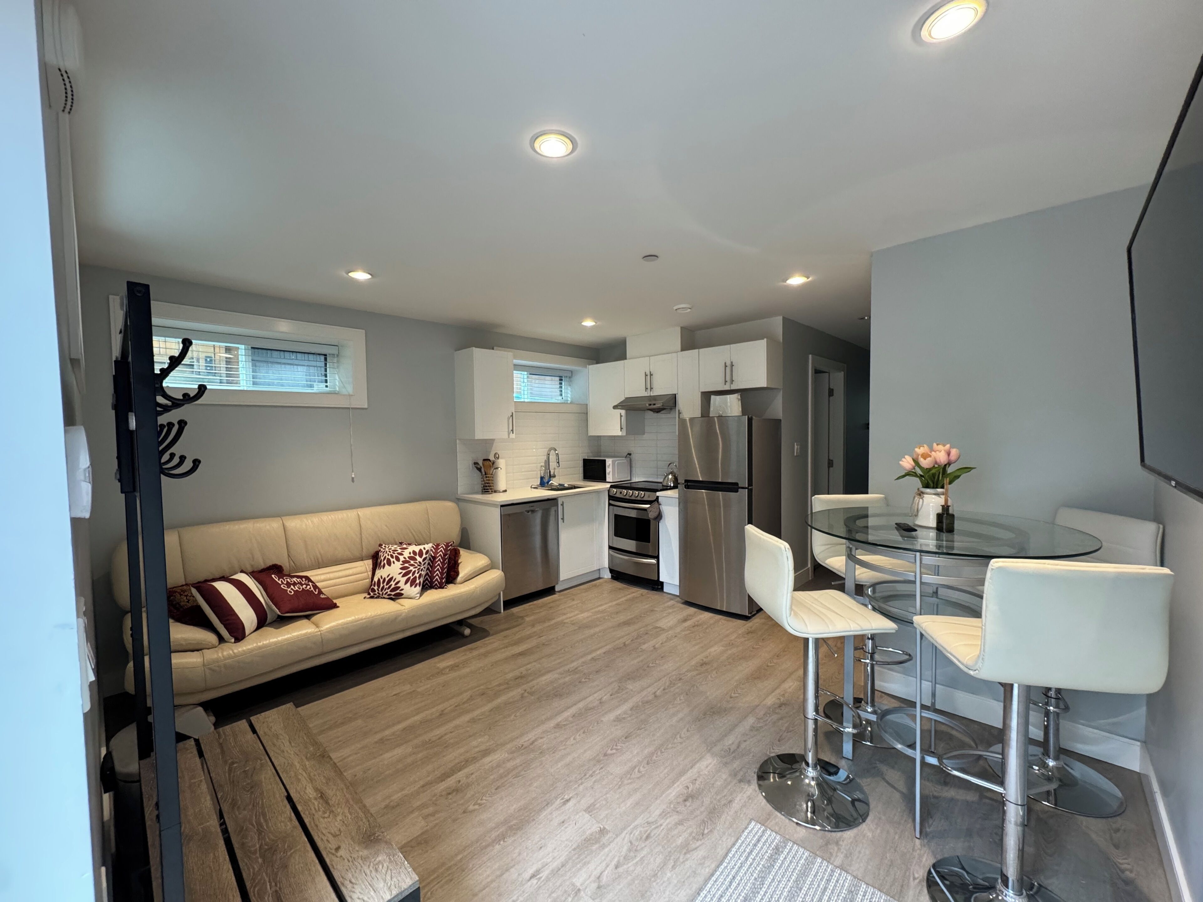 A compact living space with a kitchenette, a sofa, a dining area with bar stools, and a small table with a vase of flowers.
