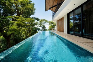 A modern building with a swimming pool, surrounded by lush greenery. - Panoramic Ocean Views • Eco-Luxury Solar Retreat with 5 bedrooms (Santa Teresa)