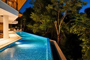 Une piscine à débordement offrant une vue sur les arbres et un bâtiment.