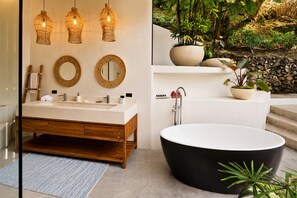 A modern bathroom with a wooden vanity, a freestanding bathtub, and a wall-mounted sink. - Panoramic Ocean Views • Eco-Luxury Solar Retreat with 5 bedrooms (Santa Teresa)