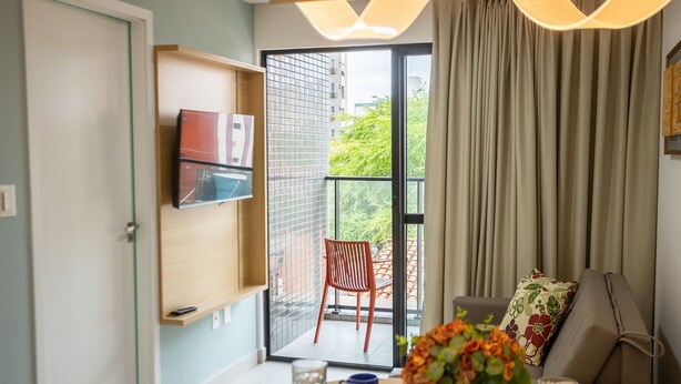 Una habitación con una mesa de comedor lista para dos personas, una silla, un televisor montado en la pared y vistas al balcón exterior.