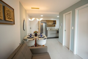 A modern kitchen with a refrigerator, a dining table with chairs, and a sofa in the foreground. - Unigreen Residence Manaira by Carpediem Close to the Beach, Manaira Shopping and MAG Shopping (João Pessoa)