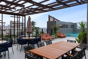 A rooftop terrace with a wooden table, blue and orange chairs, a pool, and city views. - Unigreen Residence Manaira by Carpediem Close to the Beach, Manaira Shopping and MAG Shopping (João Pessoa)