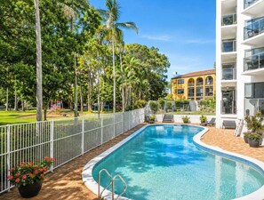 A swimming pool with a white fence, surrounded by palm trees and a building with balconies. - 2BR Riverside Retreat with Pool Near Beach (Gold Coast)