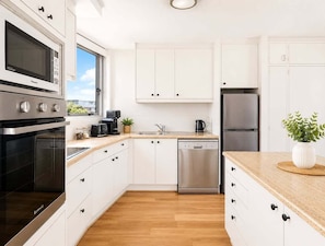 A modern kitchen with white cabinetry, stainless steel appliances, and a wooden countertop. - 2BR Riverside Retreat with Pool Near Beach (Gold Coast)