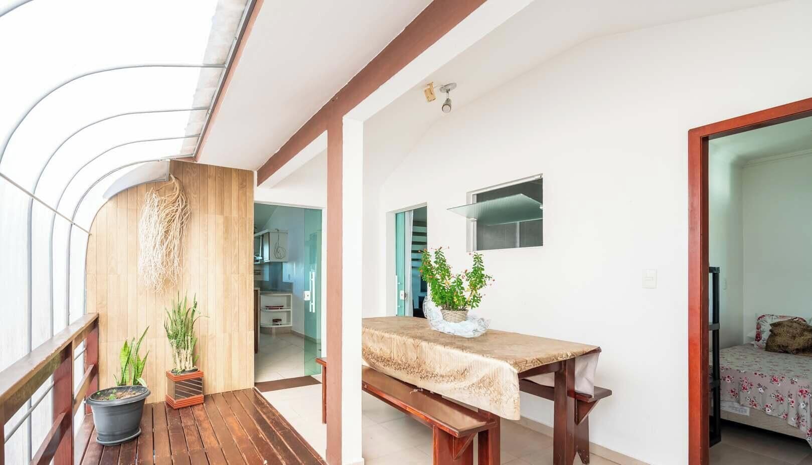 Een modern interieur met een houten eettafel, planten in potten, en een keuken zichtbaar door een open deur.