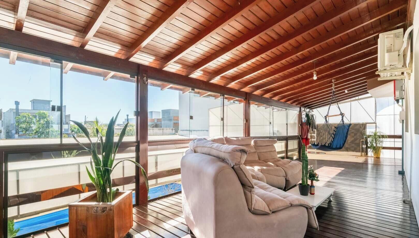 Et overdækket udendørs opholdsområde med en sofa, en hængestol og krukker med planter.