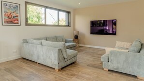 A spacious living room with a large window, a grey sofa, a smaller armchair, and a flat-screen TV mounted on the wall. - Stunning, Renovated Family Villa in Le Pouliguen (Le Pouliguen)