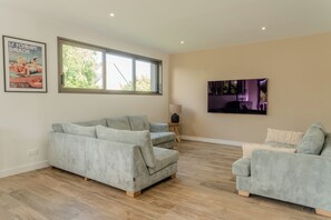 A spacious living room with a large window, a grey sofa, a smaller armchair, and a flat-screen TV mounted on the wall. - Stunning, Renovated Family Villa in Le Pouliguen (Le Pouliguen)