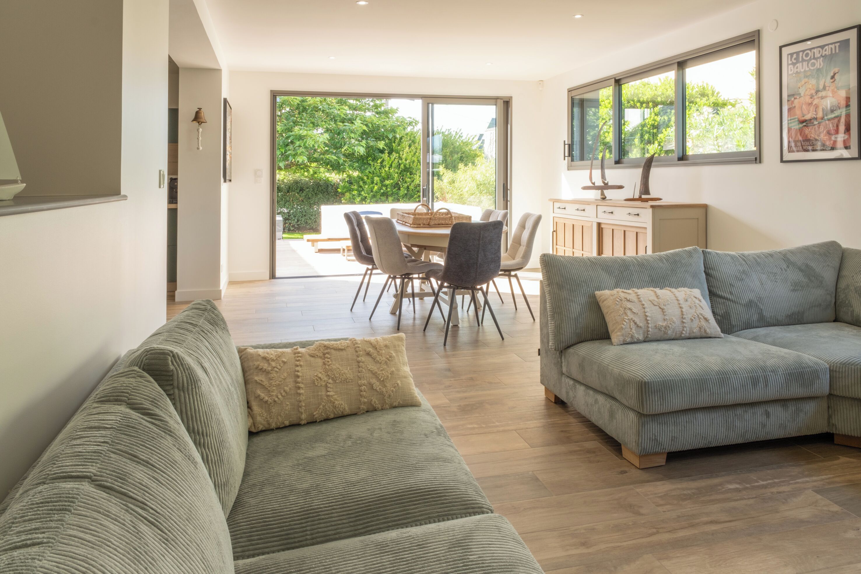 Un salon moderne avec un canapé, une table à manger et des chaises, et une vue sur l’extérieur à travers une porte vitrée.