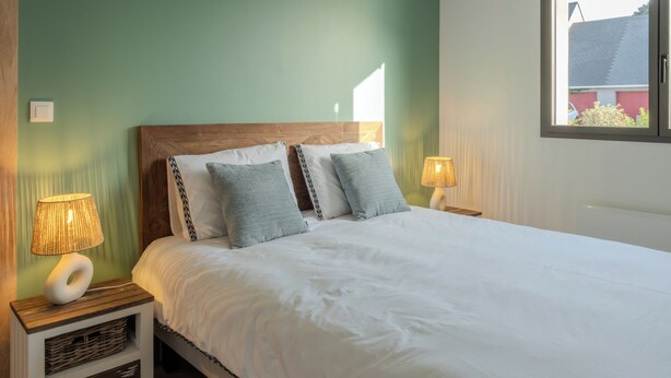 A bed with white bedding, two patterned pillows, and a wooden headboard. There are two bedside tables with lamps and a small storage drawer. - Stunning, Renovated Family Villa in Le Pouliguen (Le Pouliguen)