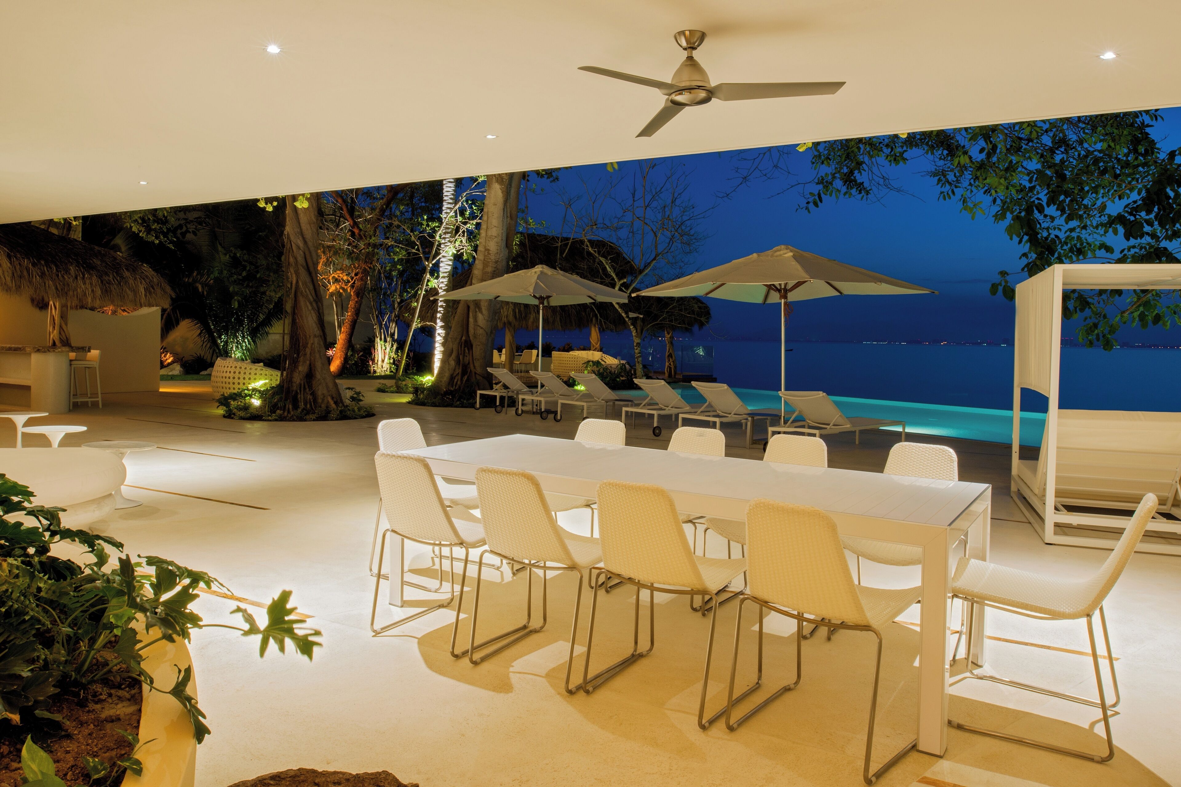 Un espace extérieur aménagé pour les repas, avec vue sur la piscine, doté de mobilier blanc et de parasols.