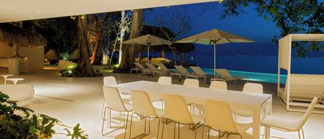 An outdoor dining area with a pool view, white furniture, and umbrellas.