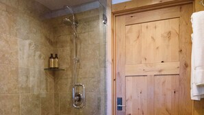 A shower with a glass door, a wooden door, and a shelf with bottles. - Modern Elkhorn Updated 2 bedroom/2 bath (Sun Valley)