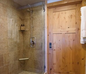 Eine Dusche mit Glastür, einer Holztür und einem Ablagefach mit Flaschen.