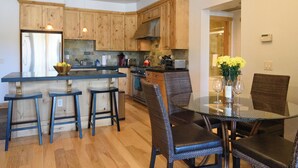 A modern kitchen with wooden cabinets, a central island, bar stools, and a dining table with chairs. - Modern Elkhorn Updated 2 bedroom/2 bath (Sun Valley)