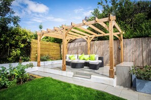 A wooden pergola with outdoor seating, a white fence, and a wooden deck. - Stylish costal escape stay with sea breeze views. (Brighton)