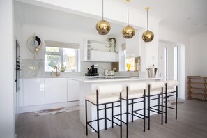 Een moderne keuken met witte kastjes, een centraal eiland met barkrukken en hanglampen.