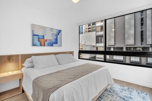 A modern hotel room with a bed, a nightstand, a window with a view of buildings, and a piece of abstract art on the wall. - Modern 2BR Miami | Rooftop Pool | Near Bayfront (Miami)
