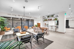 A modern interior with a dining area, seating arrangements, and a kitchen visible through a glass partition. - Dazzling 2BR Miami | Rooftop Pool & Co-Working (Miami)