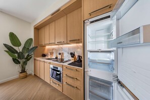 A modern kitchen with wooden cabinets, a built-in oven, and a refrigerator with a glass door. - Modern Wynwood Studio | Rooftop Pool & Gym Access (Miami)