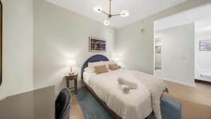 Et hotelværelse med seng, sengeborde, et skrivebord, en stol, en loftlampe og et billede på væggen.