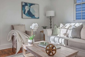 A living room with a sofa, a coffee table, a lamp, and a painting on the wall. - 1880s Charleston Single, Two bedroom with parking (Charleston)