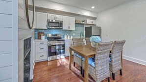 A modern kitchen with white cabinets, stainless steel appliances, and a dining area with wicker chairs and a wooden table. - 1880s Charleston Single, Two bedroom with parking (Charleston)