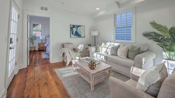 A spacious living room with a wooden floor, a sofa, a coffee table, and a large window. - 1880s Charleston Single, Two bedroom with parking (Charleston)