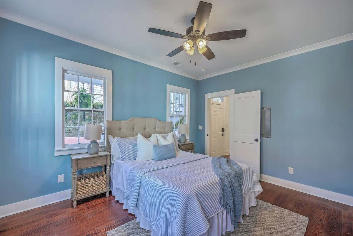 Une chambre à coucher avec un lit, un ventilateur de plafond, une table de chevet, une lampe et une fenêtre.