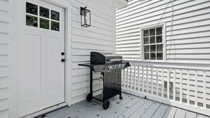 A white house exterior with a white door, a window, a black grill cart, and a white picket fence. - 1880s Charleston Single. Bermuda Suite one bedroom (Charleston)