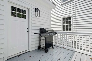 A white house exterior with a white door, a window, a black grill cart, and a white picket fence. - 1880s Charleston Single. Bermuda Suite one bedroom (Charleston)