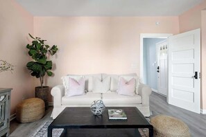 A living room with a white sofa, a black coffee table, a large potted plant, and a white door. - 1880s Charleston Single. Bermuda Suite one bedroom (Charleston)