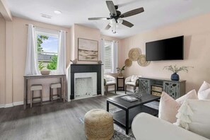 A living room with a fireplace, a ceiling fan, a TV mounted on the wall, and a seating area with a coffee table. - 1880s Charleston Single. Bermuda Suite one bedroom (Charleston)