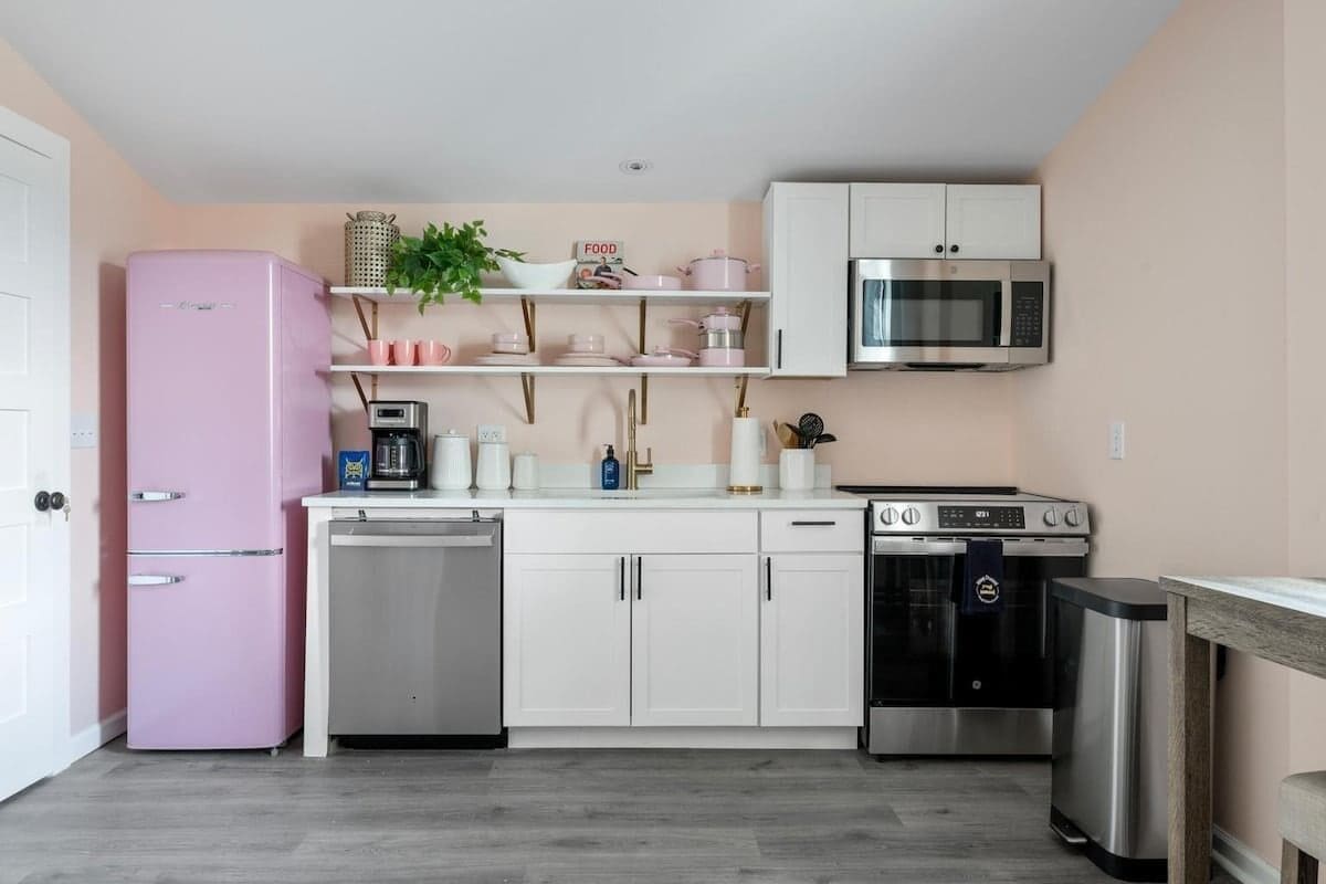 Eine kompakte Küche mit einem rosa Kühlschrank, weißen Schränken, einer Mikrowelle, einem Backofen und einem Geschirrspüler.