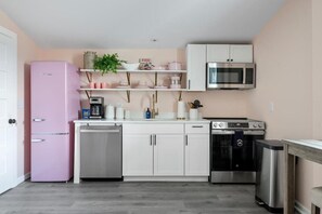 A compact kitchen with a pink refrigerator, white cabinets, a microwave, an oven, and a dishwasher. - 1880s Charleston Single. Bermuda Suite one bedroom (Charleston)