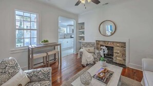 A living room with a fireplace, a ceiling fan, a dining area with a table and chairs, and a view into the kitchen. - 1880's Charleston Single. One Bedroom with parking (Charleston)